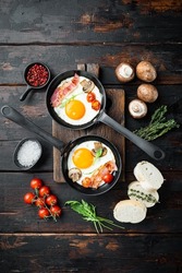 Fried eggs with bacon and vegetables set in cast iron frying pan, on old dark  wooden table background, top view flat lay
