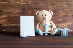 Little teddy bear toy with gift box, digit one on table with copy space. Baby shower, accessories, stuff, present for boy child first year happy birthday, newborn party background, mock up, template.