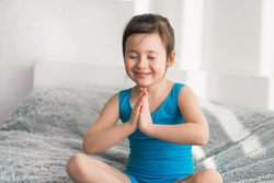 The child is sitting in the lotus position. The girl practices yoga in the morning. Girl in a blue tracksuit
