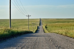 Rural gravel road lined with telephone poles going into distant open prairie in Oklahoma