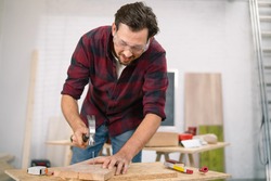 Close up of hammering a nail into board. A carpenter wearing a red flannel shirt, jeans and cloth protective gloves nails the wooden boards.