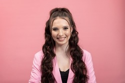 Girl in pink outfit. Portrait of smiling, happy cheerful cute young lady with long dark curly hair tied in ponytail on colorful background.