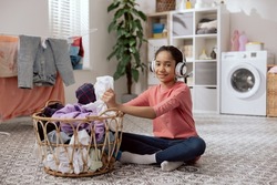 A young girl listens to music on large wireless headphones while doing household chores. A teenage girl folds laundry, separates clothes.