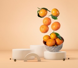 Tangerines falling into a bowl, on a podium of geometric shapes with copy space.