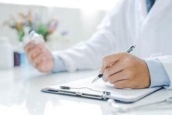 Doctor holding prescription bottle and writing prescription on a special form at office room. Healthcare, Vaccine, medical and pharmacy concept.