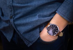 Close-up of luxury watch brown leather strap on wrist of man. Businessmen hand in pants pocket.  His wearing blue jean shirt and navy blue jeans with casual style.