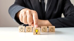 Businessman choosing light bulb icon, full of ideas and creativity on the wooden cube, financial planning ideas to achieve goals.