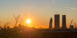 Sunrise in Milan (Italy) in backlight, with lens flares and perfect blue sky. Silhouette of towers of Citylife district in the background.
