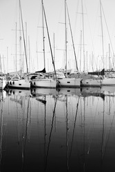 Moored sailboats reflecting their shape in the calm waters of the marina of Varazze, Liguria, Italia. Monochromatic.