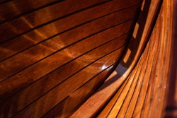 Interior abstract view of a traditional yacht constructed of highly varnished wooden planks with black caulking. Shows the construction of a craft. Beautiful red wooden tones, with interesting light