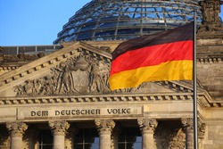 The German flag in front of the Reichstag building in Berlin. The inscription says: Dem Deutschen Volke - To the German people.