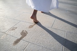 closeup perspective view of feet of child dressed in white bathing robe leaving wet footprints on stone near pool