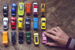 horizontal top view of male hand arranging an assorted metal colorful toy car collection on brown wooden floor in natural light