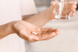 Close up woman holding pill in hand with water. Woman takes medicines with glass of water. Daily norm of vitamins, effective drugs, modern pharmacy for body and mental health concept.