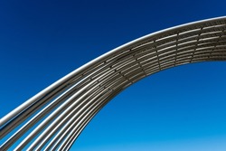 Metal tubes in public space arching in front of clear, deep blue sky.