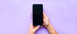 The layout of the phone. The girl holds the phone with both hands. Background lilac under the color of nails. A beautiful manicure. Flat lay.