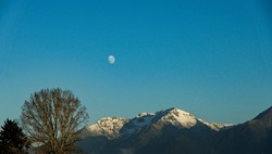 Photo of nearby snow capped mountain with the moon above it. It was taken at Te Anau, a tourist destination for glow worms and Milford Sound, in Southland New Zealand