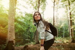 Young woman resting after a walk in the forest, carrying a backpack in the forest on sunset light in the autumn season.
