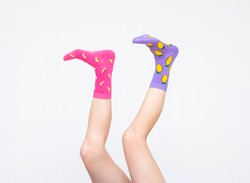 a female legs in colorful socks holding banana juggling feet isolated on white background