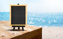 Blank blackboard on wood table food stand with blur sand beach and blue sea with bokeh light background.Template Mock up for summer vacation promotion sale