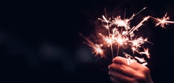 Hand holding burning Sparkler blast on a black bokeh background at night,holiday celebration event party,dark vintage tone