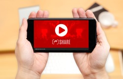 Watching two hand holding mobile phone with play and share video icon on screen and blur desk office background,Digital content concept
