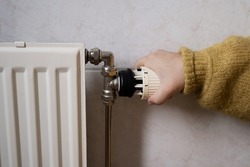 Hand turning off the heating, radiator while wearing a warm yellow sweater. Concept of saving electricity and heating as a way of energy saving consumption.