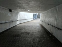 A grey, brutalist, concrete underpass leading down to a brightly lit, multi-door entrance, showing light at the end of the tunnel at Four Seasons Shopping Centre, Mansfield, UK 