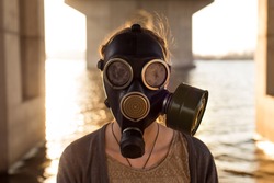 Ecological concept of air contamination. Portrait of woman in gas mask near water