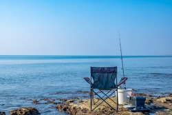 Folding camp chair for fishing and rest. Chair and fishing rod on the shore of the sea. Inventory of the fisherman