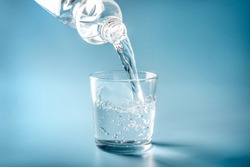 Water pouring from plastic bottle in glass on blue background