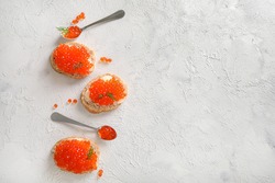 Slices of bread with red caviar and teaspoons with red caviar on plate on white background. Top view. 