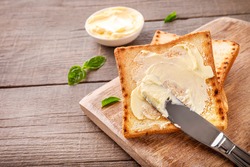 Knife spreading butter on toast bread on wooden background. Copy space.