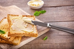 Knife spreading butter on toast bread on wooden background.