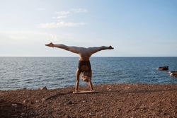 Woman practicing the handstand yoga position with the legs open in front of the sea