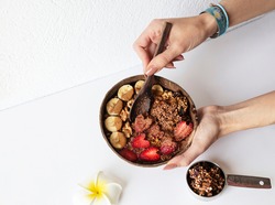 Woman holding coconut plate with tasty granola bowl. banana and strawberry. Close up. Healthy food and tropical style. Top view.