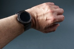 Smart watch with a black screen on a man's hand, close-up on a gray background.
