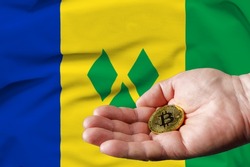 Golden bitcoin coin in man's hand, Saint Vincent and the Grenadines flag in the background.