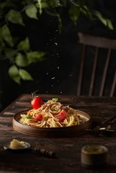 Homemade Italian spaghetti pasta with sauce, tomatoes, basil and parmesan. Traditional Italian cuisine. Served on a dark table with a rustic wooden background. Vertical