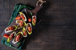 Endive salad boats filled with pico de gallo over minced beef served on a rustic cutting board on a dark wooden background, horizontal orientation, top view, copy space