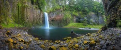 A woman sitting on the rock at Beautiful waterfall of Abiqua Creek, Abiqua Falls. Abiqua Falls is one of the hidden gems in Oregon. Abigua falls flowing over the lava rock formation