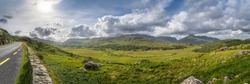 Large panorama with road in Molls Gap, Owenreagh River valley, MacGillycuddys Reeks mountains and farms, Wild Atlantic Way, Ring of Kerry, Ireland