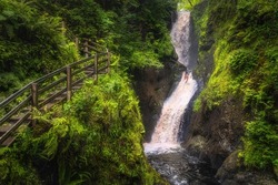Spectacular wooden boardwalk on the hill with a view on tall waterfall and river in majestic Glenariff Forest Park, Antrim, Northern Ireland