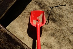 Sandbox playground for kids, with a red plastic shovel inside of it