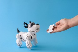 Robot dog pet on light blue background with human hand giving bone