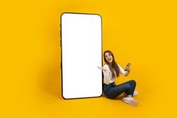 Woman demonstrate big empty screen smartphone mockup. Great mobile offer, application concept idea image. Caucasian excited smiling attractive girl sitting near big huge mobile phone. Copy space.