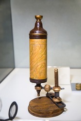 Antique Leeuwenhoek microscope in light brown on a white table, Microbiology scientific instruments.