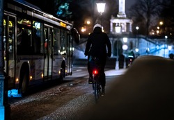 A cyclist riding alongside the bus in the illuminated city at night