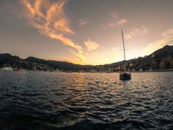 A sail boat sailing in the sea surrounded by high rocky mountains under the sunset sky in Catalina Island, CA
