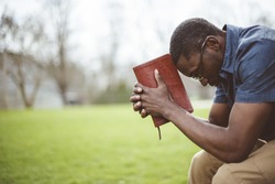 A young African-American male sitting with closed eyes with the Bible in his hands